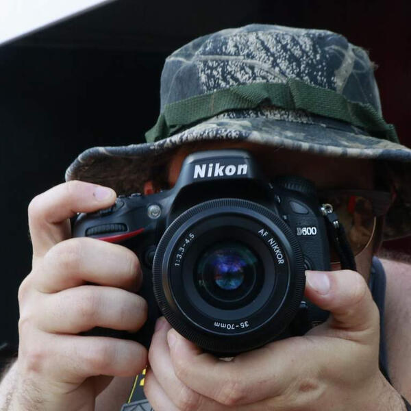 photographer with a nikon camera takes a picture facing right at you
